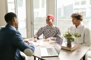 Three professionals meeting in a sunny office discussing finance with smiles.