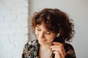 A joyful woman with curly hair enjoys music indoors using wireless earphones.