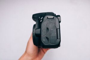 Detailed side view of a DSLR camera held by a hand on a white background.