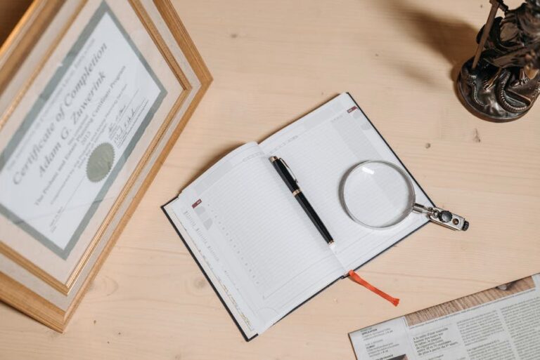 A tidy workspace featuring a certificate, open journal, magnifier, and statue on a wooden desk.