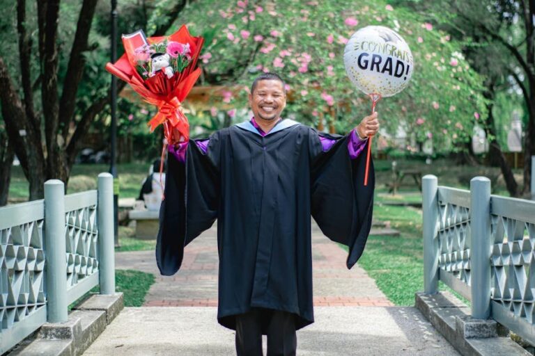 Man celebrating graduation with flowers and balloon outdoors in a park.