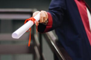 A close-up image of a graduate holding a diploma tied with a red ribbon, symbolizing achievement and success.