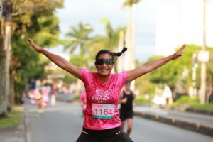 Smiling woman celebrates crossing the finish line in a 10K race, arms raised in triumph.