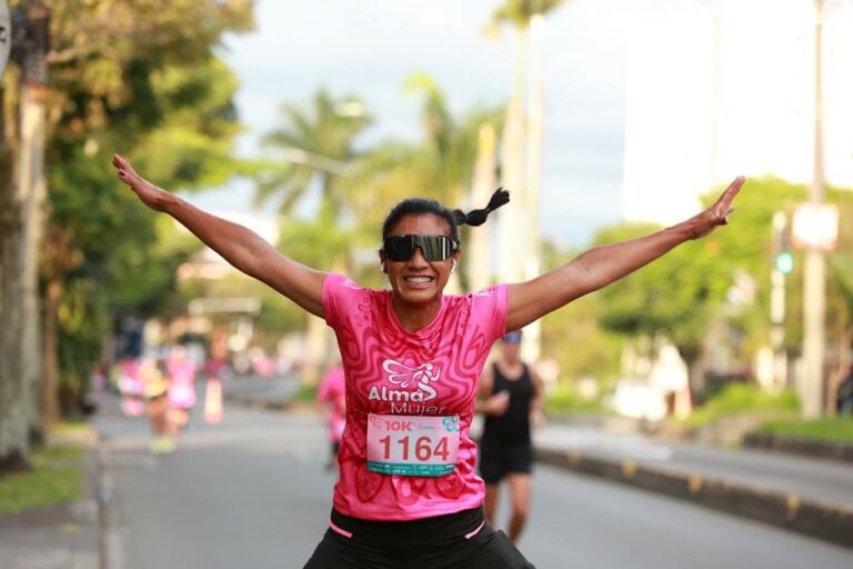 Smiling woman celebrates crossing the finish line in a 10K race, arms raised in triumph.