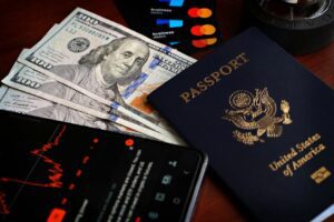 US passport with hundred-dollar bills, credit cards and smartphone showing stock data.