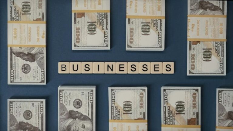 Bundles of US hundred-dollar bills and Scrabble tiles spelling 'businesses' laid out creatively.