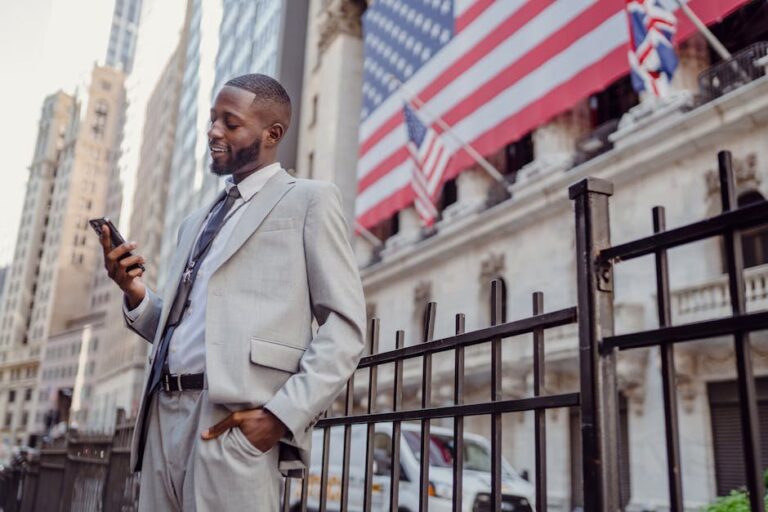 African American businessman smiling while checking his phone on a city street in New York.