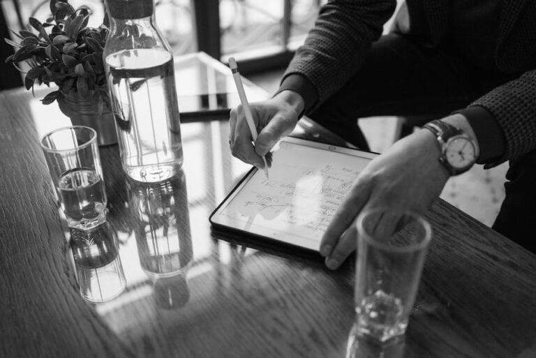 A close-up of a person using a stylus on a tablet, with a modern workspace setting.