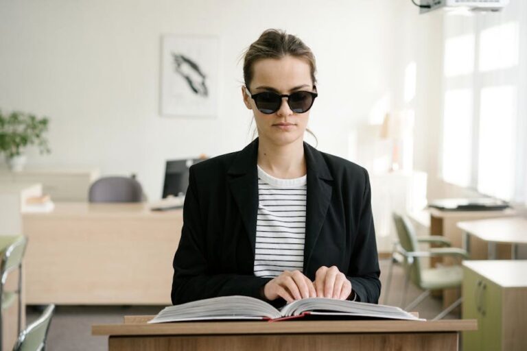 A blind woman in sunglasses reading a braille book at an office desk, signifying empowerment.