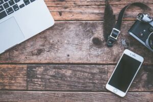 Flat lay of a laptop, smartphone, and camera on a rustic wooden desk, featuring modern technology and vintage charm.