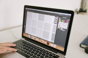 A laptop displaying graphic design patterns with a hand interacting, ideal for creative workspace themes.