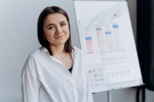 Smiling woman in a white shirt presents business graphs on a flipchart in a modern office.