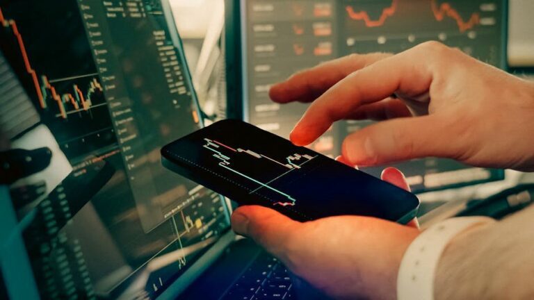 Hands interact with smartphone for analyzing cryptocurrency trading on digital screens.
