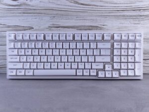 Sleek wireless white keyboard displayed on a textured wooden background, ideal for office or tech setups.