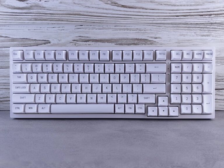Sleek wireless white keyboard displayed on a textured wooden background, ideal for office or tech setups.