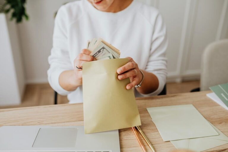 Close-up of person holding envelopes with cash at a wooden desk indoors.