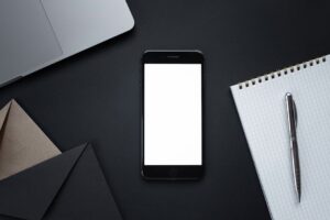 A sleek flat lay of a smartphone, notebook, pen, and laptop on a dark surface, ideal for modern office themes.