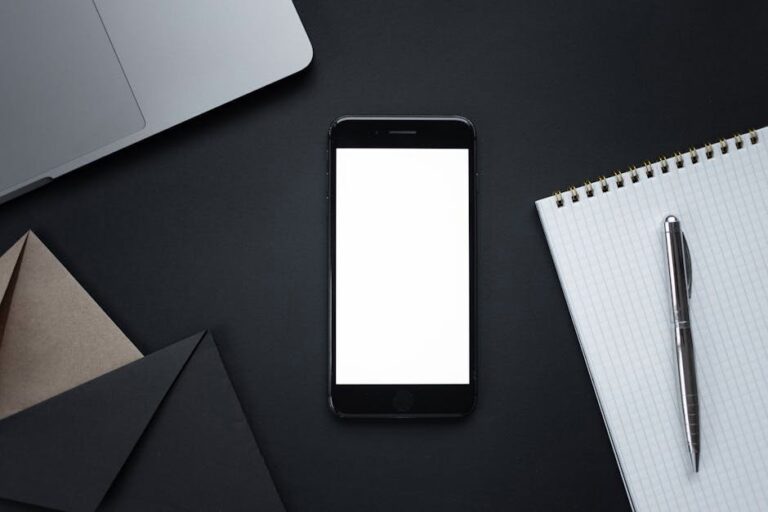 A sleek flat lay of a smartphone, notebook, pen, and laptop on a dark surface, ideal for modern office themes.