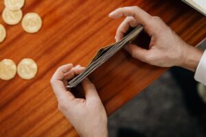 Close-up of hands counting currency with coins scattered on a wooden table. Perfect for finance and business themes.