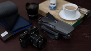 A close-up view of tech gadgets including a camera and drone, paired with a coffee cup on a desk, highlighting modern lifestyle.